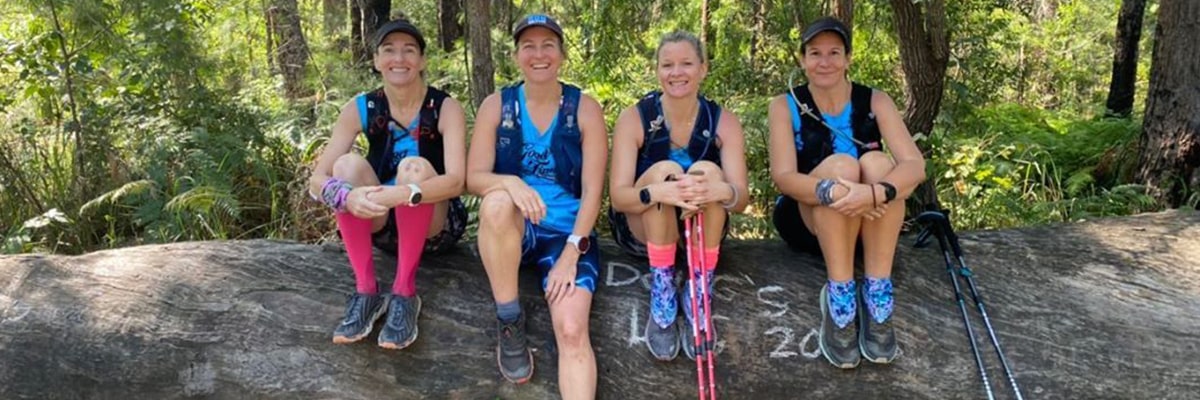 Four ladies rest on a log in the Australian bush while completing the Kokoda Virtual Challenge