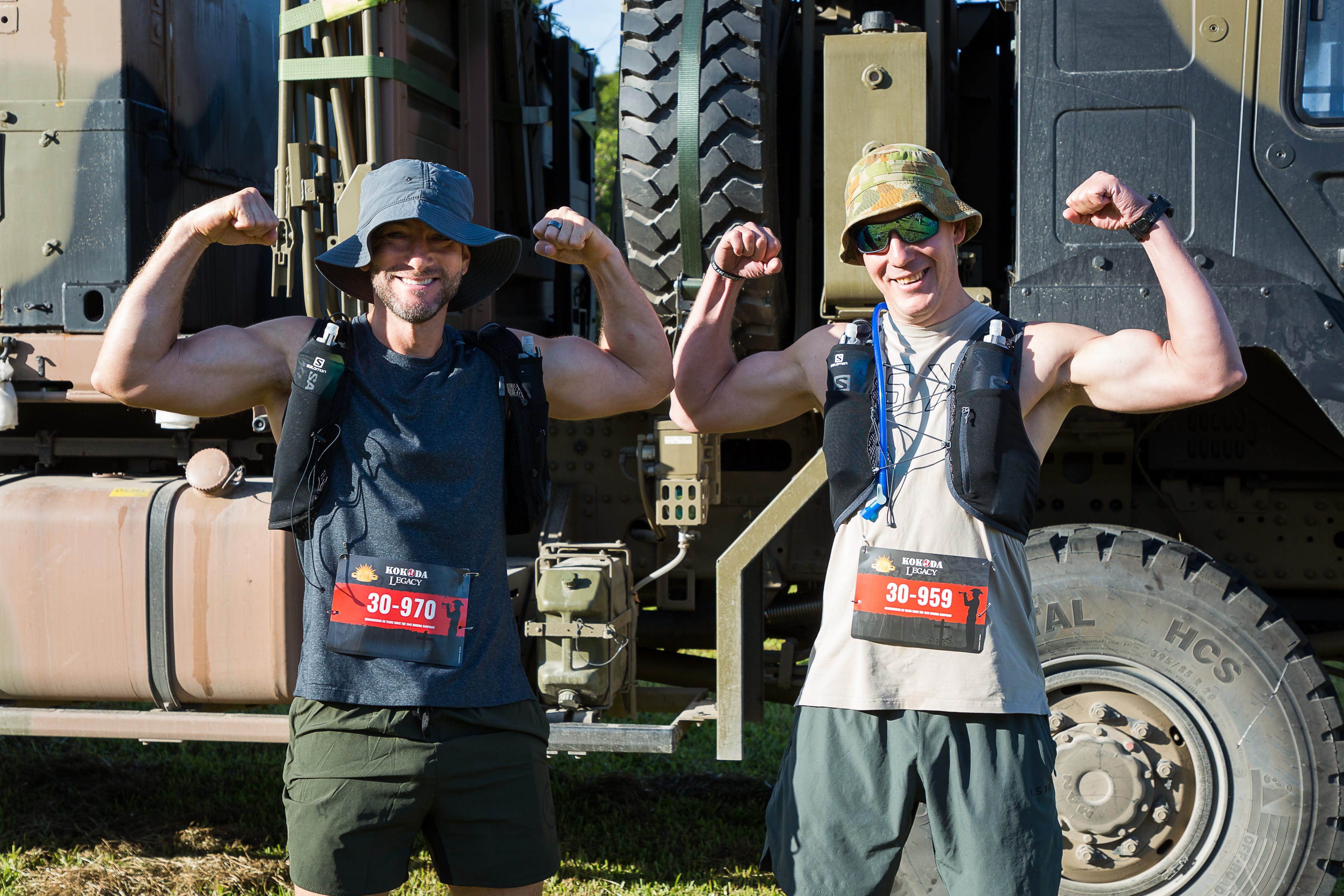 Two men flexing their biceps in front of an army vehicle at the Kokoda Legacy start line